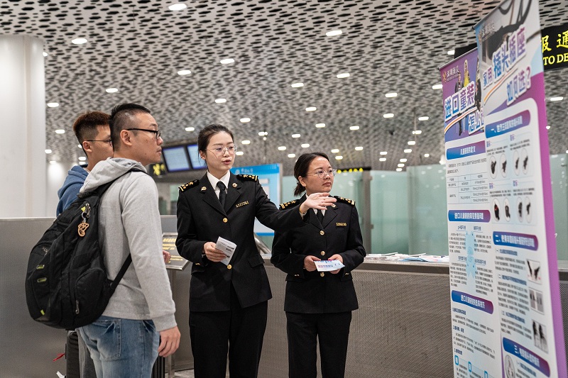图为：关员在航站楼向进境旅客普及消费品选购常识